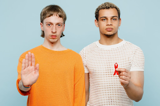 Young gay men couple holding red HIV awareness ribbon and a stop gesture, representing prevention and awareness.